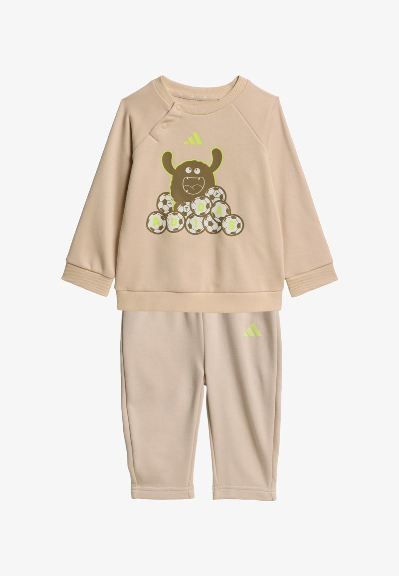 Survêtement beige pour tout-petit avec un haut à manches longues présentant un monstre de dessin animé, des ballons de football formant le mot "ADIDAS" et un pantalon assorti avec logo.