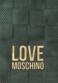 Grüner strukturierter Hintergrund mit einem Schachbrettmuster; in der Mitte befindet sich der fettgedruckte, goldene Schriftzug "LOVE MOSCHINO".