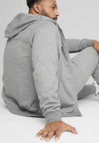 Sivá mikina na zips s kapucňou, dlhými rukávmi a voľným strihom, spárovaná s nohavicami z jemnej textúrovanej látky.