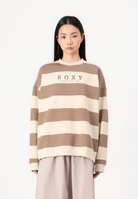 Brun og kremstripet genser med rund hals og løs passform. Har teksten "ROXY ETABLERT 1990" på forsiden.