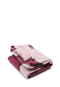 Coperta piegata in tonalità di bordeaux e rosa pallido, con un motivo astratto a tie-dye. I bordi sono frangiati, aggiungendo texture.