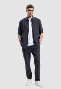 Korte ærmer mørkegrå skjorte med to brystlommer over en hvid T-shirt, parret med mørkegrå bukser og hvide sneakers.