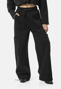 Zwarte wijde cargo broek gemaakt van zachte stof, met twee grote zijzakken met rode stiksels, een elastische tailleband en een trekkoorddetail.