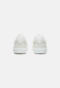 Weiße Sneakers mit einem Obermaterial aus glattem Leder und Wildleder, flachen Schnürsenkeln, strukturierten Akzenten und einer dicken weißen Gummisohle.