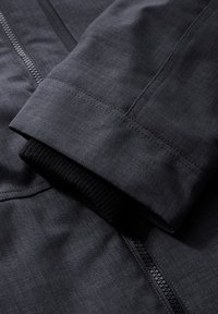 Black jacket with a smooth, textured fabric. Features a zip closure and a knitted cuff. Close-up view highlights stitching details.