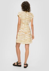 Robe à manches courtes ceinturée en beige clair avec des rayures blanches en zèbre, présentant une coupe décontractée et un tissu texturé. Accentuée par une fermeture à bouton dans le dos.
