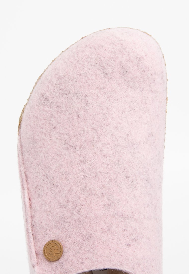 Chausson en feutre rose avec un bout arrondi et une surface texturée. Comprend un accent logo circulaire sur le côté. Semelle en liège visible en dessous.