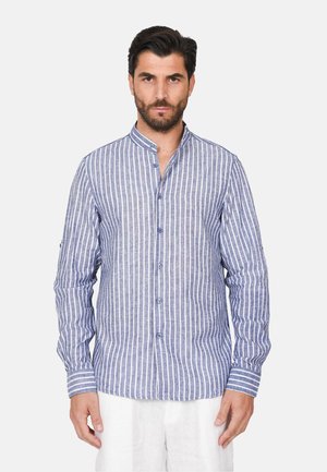 Uomo che indossa una camicia a righe verticali blu e bianche con bottoni, maniche lunghe e colletto alla coreana, abbinata a pantaloni bianchi.