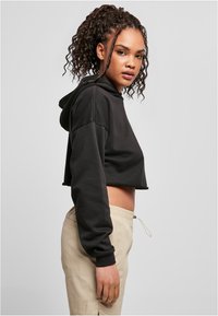 Patogus juodas hoodie su ilgomis rankovėmis ir raišteliu, derinamas su šviesiai rudos spalvos raištelių kelnėmis, pagamintomis iš glotnaus, lengvo audinio.