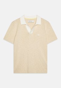 Polo shirt beige lavorato a maglia con colletto bianco e scollatura a V. Presenta maniche corte e un piccolo logo sul lato sinistro del petto. Texture morbida.
