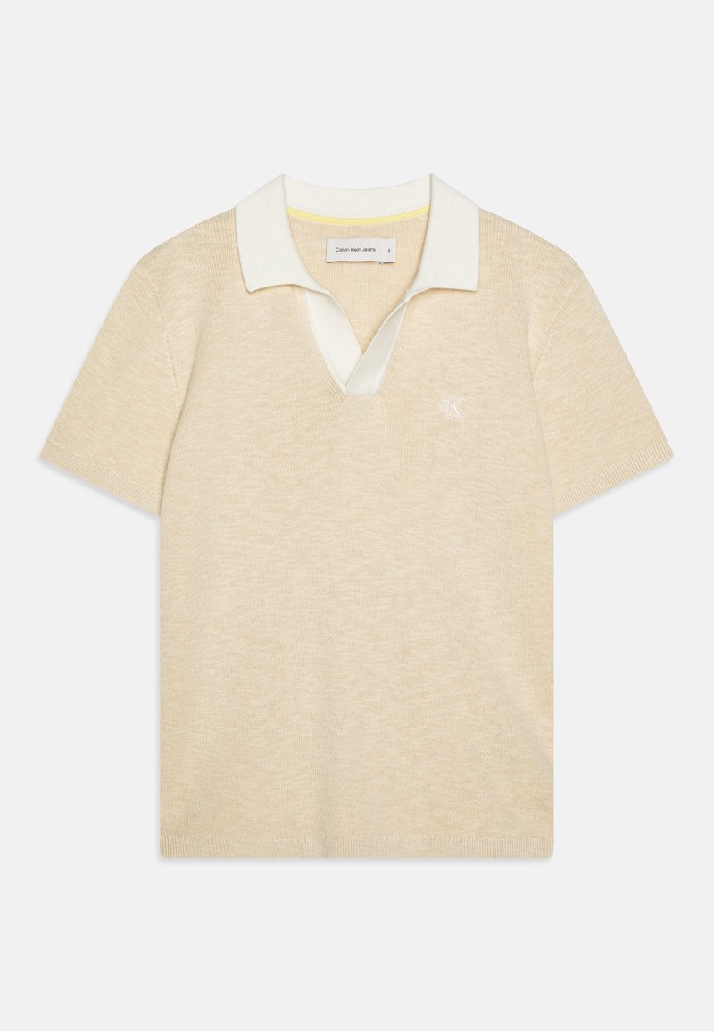 Polo shirt beige lavorato a maglia con colletto bianco e scollatura a V. Presenta maniche corte e un piccolo logo sul lato sinistro del petto. Texture morbida.