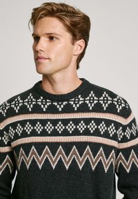 Maglione lavorato a maglia verde scuro con motivi geometrici bianchi e beige, scollo a coste e dettagli zigzag all'orlo.