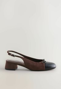 Brūnas zamšaina slingback kurpe ar melnu ādas purngalu, ar zemu blokkāju un dekoratīvu loku priekšpusē.