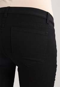 Black denim jeans feature a fitted design with a smooth texture, a back pocket, and a classic waistband without visible hardware accents.