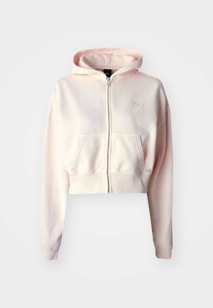 Vaaleanpunainen vetoketjullinen huppari, sininen urheiluliivi ja shortsit, istuu vihreällä alustalla. Silkkiset pinnat, rento istuvuus ja urheilullinen design.