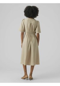 Vestido midi beige con mangas cortas, detalle de cintura fruncida y un corte holgado. La tela tiene una textura sutil que complementa el diseño.