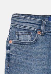 Denimjeans i lys blå farge med standard midje, frontlomme med kobberbeslag og en teksturert stofffinish.