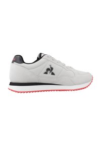 Zapatillas de deporte gris claro con acabado de ante, acentos en negro y suela de goma roja. Presenta un logo en el lateral y un diseño de cordones.