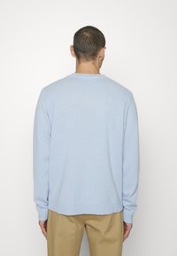 Pull en maille bleu clair à manches longues, col et ourlet côtelés. Présente une coupe décontractée et une texture subtile. Porté avec un pantalon beige clair.