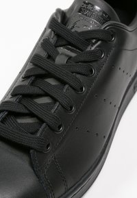 Svart lädersneaker med texturerad yta, snörningsdesign, perforerade detaljer på sidorna och en slät sula. Har svarta snören och logotyp.