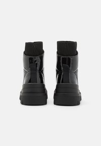 Bottines en cuir verni noir avec un bord côtelé extensible, semelle épaisse et tirette arrière. Fini lisse avec un design minimaliste.