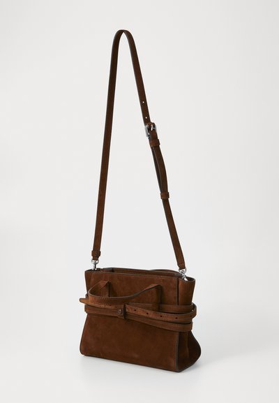 Brūnas zamšādas crossbody soma ar taisnstūra formu, ar platām siksnām, pogu aizdari un dekoratīvu loku priekšpusē.