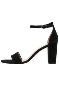 Sandales à talons hauts en suede noir avec un talon carré, bout ouvert et une bride à la cheville ornée d'une boucle en argent. Texture lisse et design minimaliste.