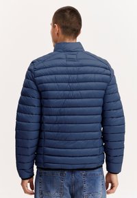 Marineblå dunjakke med quiltet design, høy krage og lange ermer. Materialet ser glatt og lett ut.