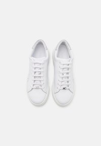 Baskets en cuir blanc avec une texture lisse, dotées de lacets plats, d'accents perforés et d'un détail en logo argenté sur le côté.