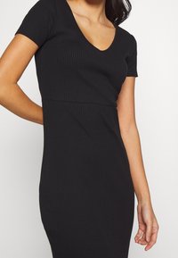 Schwarzes geripptes Kleid mit kurzen Ärmeln und einem V-Ausschnitt. Figurnah geschnitten mit einer glatten Textur und subtilen vertikalen Linien. 