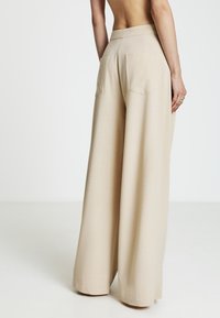 Pantaloni beige a gamba larga realizzati in tessuto leggero, caratterizzati da una texture liscia, vita alta e due tasche posteriori.