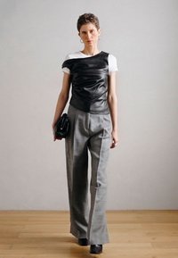 Top de couro preto sem mangas sobreposto a uma t-shirt branca, combinado com calças cinza de cintura alta e botins pretos de salto.