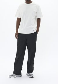 Weißes kurzärmeliges T-Shirt mit Rundhalsausschnitt, kombiniert mit lockeren schwarzen Hosen. Graue Sneaker mit Mesh- und Gummielementen runden das Outfit ab.