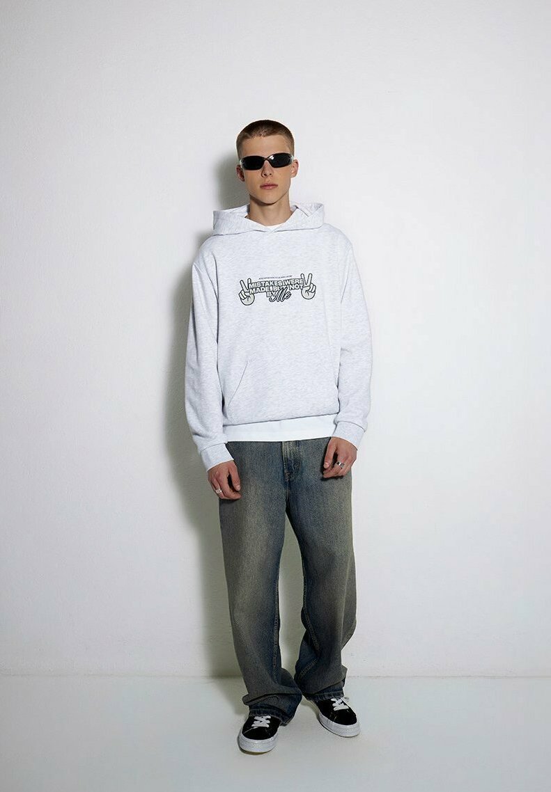 Szara bluza z kapturem z graficznym napisem, zestawiona z luźnymi dżinsami. Biały pasek i czarne sneakersy dopełniają strój.
