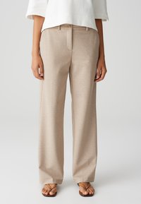 Lichtbeige wijde broek van zachte stof, met een platte voorkant, twee voorzakken en een knoopsluiting. Gecombineerd met zwarte slippers.