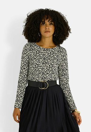 Top de manga larga con estampado de leopardo en blanco y negro, combinado con una falda negra plisada y hebilla de cinturón redonda dorada. Tejido texturizado.