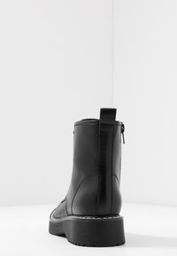 Zwarte leren enkelboots met een gestructureerde afwerking, voorzien van een ritssluiting en een stevige rubberen zool. Inclusief een trekband aan de achterkant.