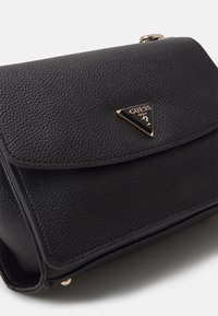 Sac à main en cuir noir texturé avec un logo triangulaire doré sur le devant. Il présente une fermeture à rabat et des détails de couture subtils.