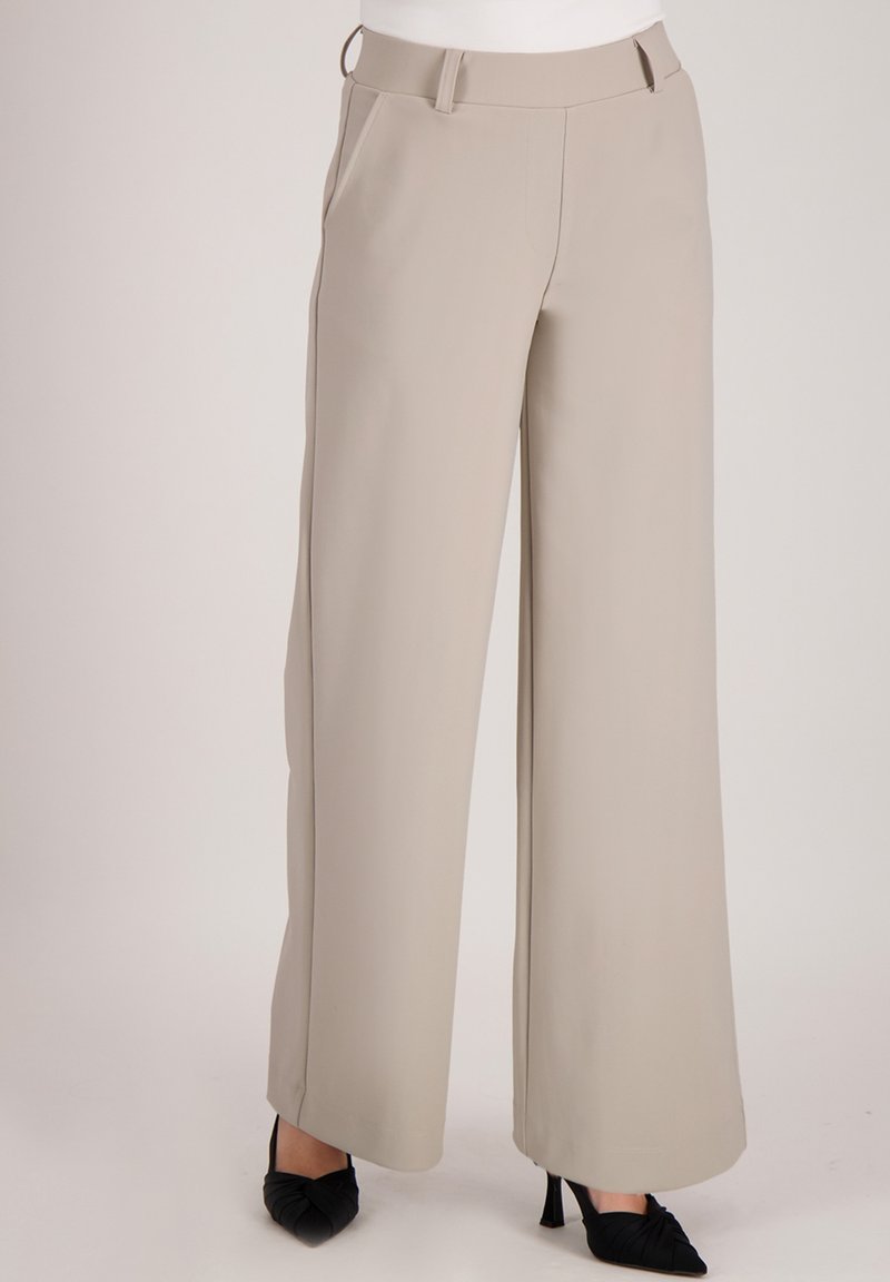 Beige wijduitlopende broek gemaakt van een gladde stof, met een tailleband op middelhoogte, zijzakken en een strakke, op maat gemaakte snit.