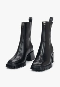 Black leather ankle boots with a high block heel, featuring a front zipper, smooth texture, and a rugged rubber sole with tread detail.