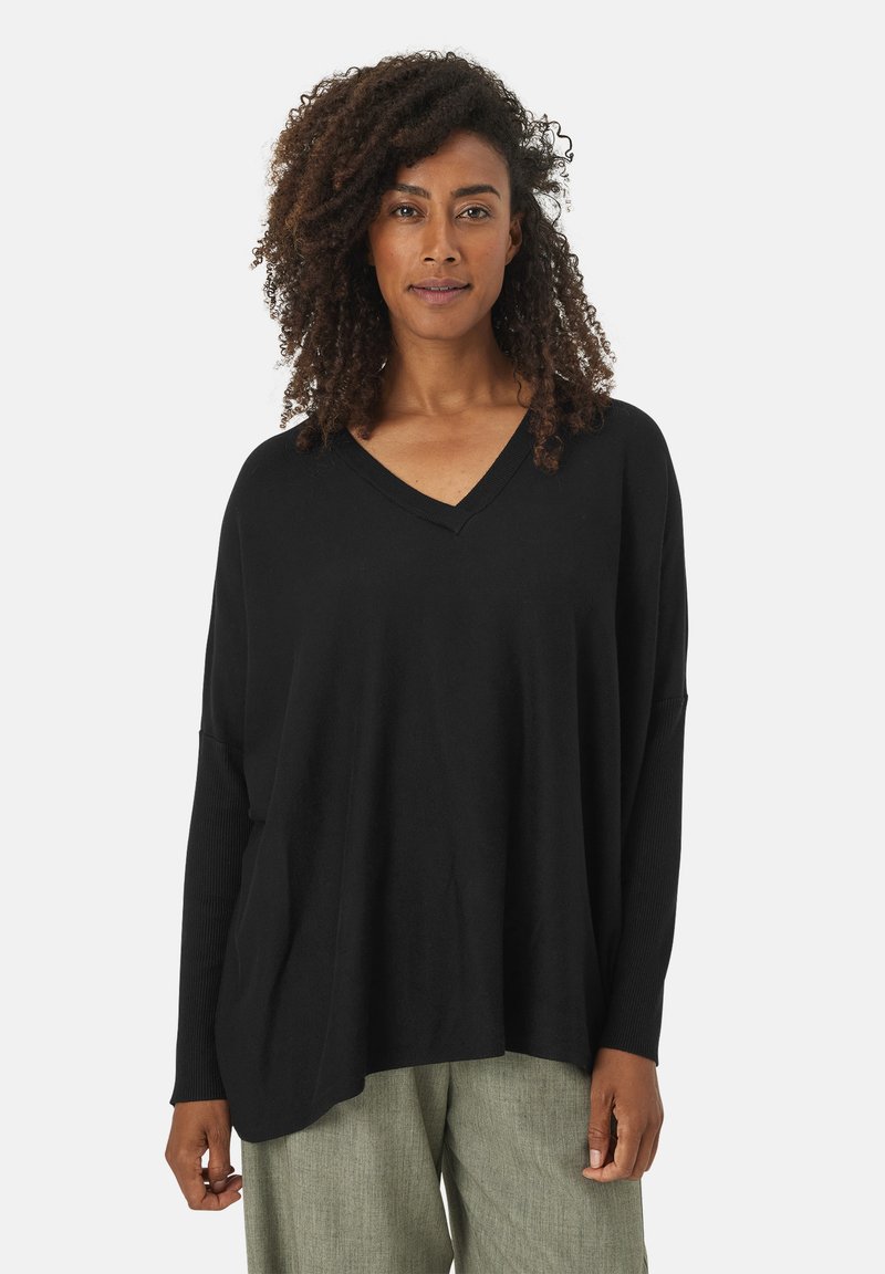 Zwarte V-hals trui met een relaxte fit, geribbelde manchetten en een zachte textuur. Gemaakt in combinatie met lichtgroene textured broek, gepresenteerd op een neutrale achtergrond.
