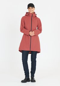 Rød vandtæt jakke med en snøret hætte, fuld lynlås og sorte detaljer, parret med mørke denimbukser og sort fodtøj.