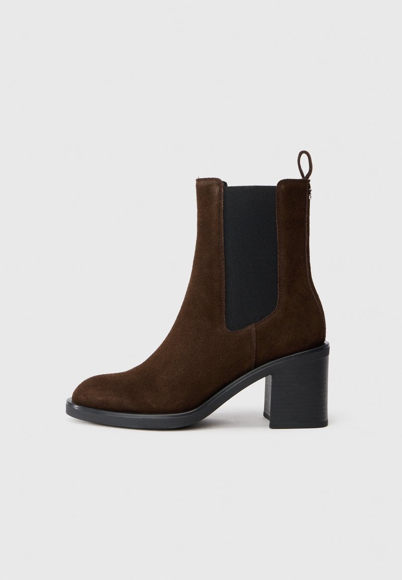 Bottine en daim marron avec talon bloc, panneau latéral élastique noir, bout arrondi et languette à l'arrière.