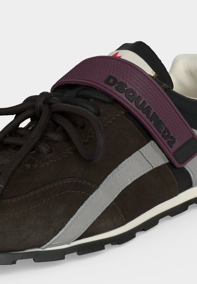 Gros plan d'une basket marron avec une bande blanche, des lacets noirs et une bride bordeaux étiquetée DSQUARED2 sur le dessus.