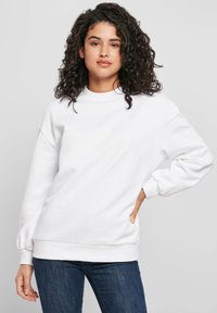 Valkoinen puuvillainen collegepaita pyöreällä pääntiellä, resorit hihansuissa ja helmassa. Mallissa on laskettu olkapää ja rento istuvuus. Yhdistetty sinisiin farkkuihin.