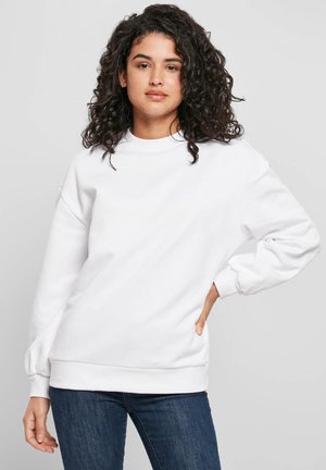 Valge puuvillane dressipluus ümara kaelusega, soonikkoes mansettide ja äärega. Omadusteks langevad õlad ja lõõgastusstiilne lõige. Kandmisega koos siniste teksadega.