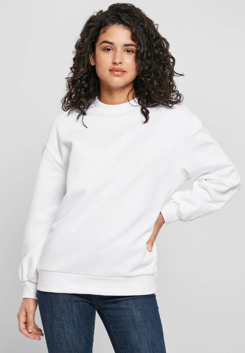 Valkoinen puuvillainen collegepaita pyöreällä pääntiellä, resorit hihansuissa ja helmassa. Mallissa on laskettu olkapää ja rento istuvuus. Yhdistetty sinisiin farkkuihin.