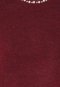 Maglione a coste bordeaux con una fila di piccole perle bianche lungo il collo. Texture morbida con un motivo a coste in tutto il capo.