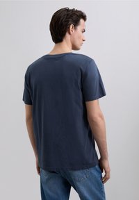 Camiseta de algodón azul marino con cuello redondo, mangas cortas y un corte holgado. Costuras visibles y textura suave. Combinada con vaqueros de color azul claro.