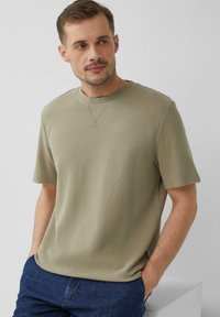 Olijfgroene t-shirt met korte mouwen, gemaakt van gestructureerde stof, met een ronde halslijn en subtiele stikdetails bij de kraag.